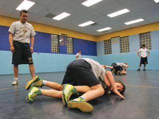Henderson Youth Wrestling coach Tony Medina, left, looks on as Brady Bransum, 9, and Cole Cauley, 7, bottom, spar during a practice at the Foothill High school wrestling room.
