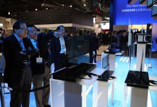 Show-goers look over ultra-thin OLED televisions at a Samsung booth at CES Thursday in Las Vegas.  Samsung unveiled OLED television prototypes with screens ranging from 14 to 31 inches. 