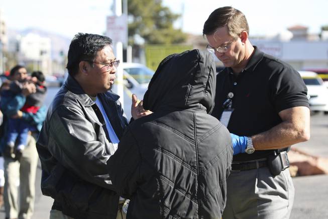 Metropolitan Police Officer Clifford Mogg, right, speaks with potential witnesses in the death of Dr. Edna Makabenta on Monday. The two being interviewed had been parked in front of the doctor's West Charleston office, where a police said a patient killed the doctor then killed himself.