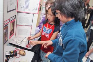 Fifth-grader Cristobal Lledo demonstrates the conduction of electricity using fluids, fruits and vegetables for third-grader Tina Ngo, right, during the fifth-grade science fair at Selma Bartlett Elementary School.
