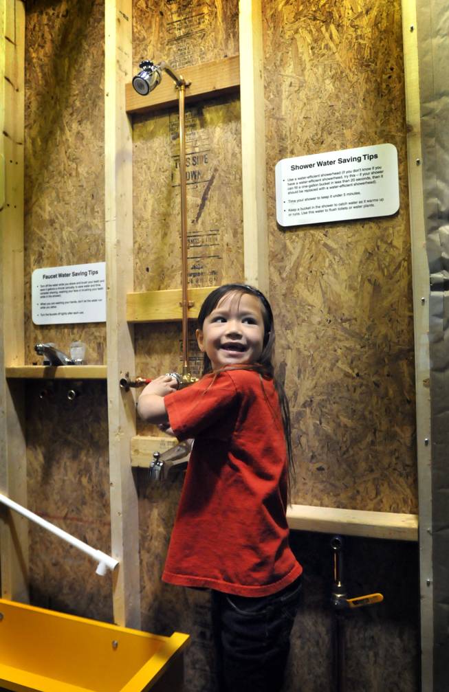 First-grader Kalai Furado, from the Green Valley Christian School, pretends to take a shower inside a plumbing display at new Green Village display at the Lied Discovery Children's Museum on Tuesday. The new 3,500 square-foot mini-city has an environmentally friendly focus that includes exhibits with lessons in everyday living and environmental sustainability.