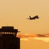 A control tower at McCarran International Airport is silhouetted against a sunset as an aircraft takes off.