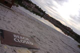 A sign indicating the beach is closed rests on the shore of Lake Las Vegas.