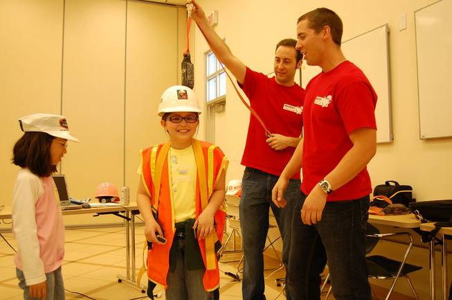 Zach Roether and Geoffrey Godzik of McCarthy Building Companies help Olivia Smistad try on construction safety gear.