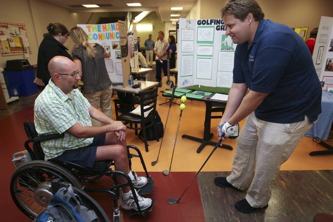 Steven Henrie lines up a putt while demonstrating his golfing grip invention for Cameron Stay, left, Thursday during the annual student Assistive Technology Fair at Touro University.