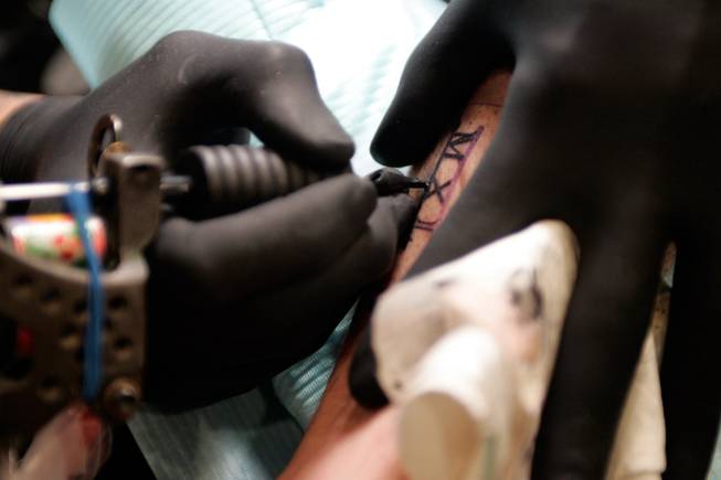 Get the point: Eric "Big E" Pele, of Huntington Ink at the Palms, gives Bill Duffey of Boston a tattoo on July 10. Despite the increasing popularity of tattoos, most companies have policies that prohibit visible body art and piercings. 