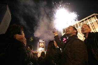 Jimmie Gleeson, center, and Blair Hanloh smile and take photos as fireworks explode off Planet Hollywood as they ring in the new year on the Strip.