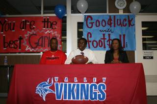 Flanked by his parents Garic and Kim Wharton, Valley High's Garic Wharton II prepares to sign his letter of intent to play football at Arizona.
