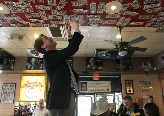 Senate candidate John Chachas tapes a dollar bill to the ceiling at the Flying Pig Bar-B-Q in Winnemucca during a swing through Northern Nevada on the Lincoln Day dinner circuit Saturday, Feb. 20, 2010.