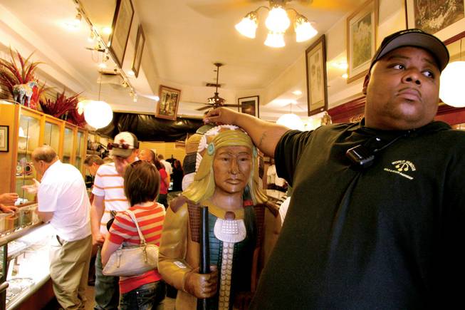 A security guard, Antwaun Austin, rests his hand on a wooden statue while keeping an eye on tourists coming into the store.