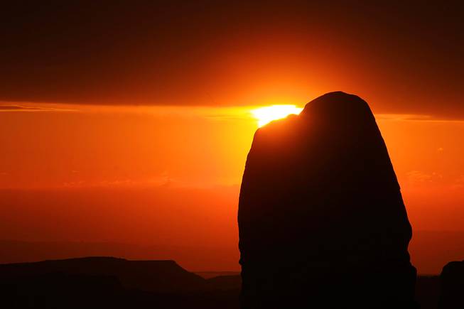 The sun is seen setting behind a rock at Arches National Park.
