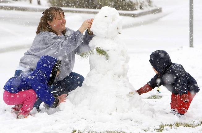 Janise Way builds a snowman with her daughter Jillian, left, and son Joey, right, during a snowstorm at Mountain Ridge Park on Friday, Jan. 7, 2004. 