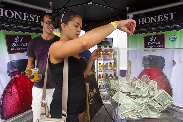 Isil Soylu of Turkey drops dollar bills into a box at a self-service Honest Tea kiosk on the Las Vegas Strip Monday, Aug. 13, 2012. Observers from the tea company watched from a distance and recorded how many people paid for the tea and how many did not. The Honest Cities social experiment is being held in 50 locations in 30 cities.