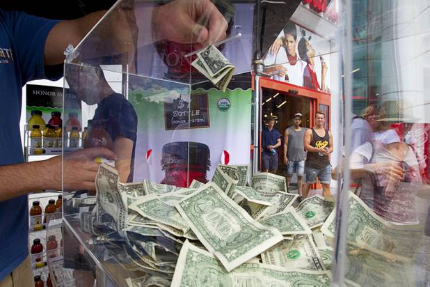 A man drops a dollar bill into a box as he buys a bottle of tea at a self-service Honest Tea kiosk on the Las Vegas Strip Monday, Aug. 13, 2012. Observers from the tea company watched from a distance and recorded how many people paid for the tea and how many did not. The Honest Cities social experiment is being held in 50 locations in 30 cities.