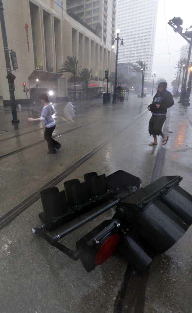 Pedestrians pass a fallen traffic light as Hurricane Isaac makes landfall, Wednesday, Aug. 29, 2012, in New Orleans, La. Isaac was packing 80 mph winds, making it a Category 1 hurricane. It came ashore early Tuesday near the mouth of the Mississippi River, driving a wall of water nearly 11 feet high inland and soaking a neck of land that stretches into the Gulf. The storm stalled for several hours before resuming a slow trek inland, and forecasters said that was in keeping with the its erratic history. The slow motion over land means Isaac could be a major soaker, dumping up to 20 inches of rain in some areas.  (AP Photo/Eric Gay)