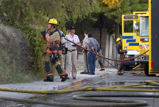 A firefighter pulls a hose as firefighters mop up after a fire that damaged six homes in a neighborhood near Washington Avenue and Pecos Road Sunday, Sept. 23, 2012. Firefighters from the City of Las Vegas Fire Department, Clark County Fire Department, North Las Vegas Fire Department responded to fight the fires. Four people suffered injuries. One cat was killed.