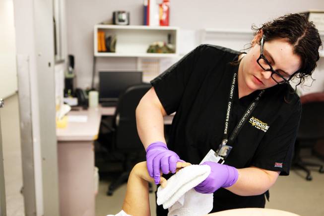 Forensic assistant Lindsay Hanes cleans the hands of a decedent, prepping to take fingerprints upon its arrival at the Clark County Office of the Coroner/Medical Examiner in Las Vegas.