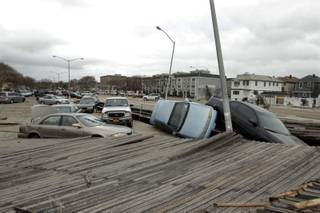Pedestrians walk past the boardwalk and cars displaced by superstorm Sandy, near Rockaway Beach in the New York City borough of Queens Tuesday, Oct. 30, 2012, in New York. Sandy, the storm that made landfall Monday, caused multiple fatalities, halted mass transit and cut power to more than 6 million homes and businesses. (AP Photo/Frank Franklin II)