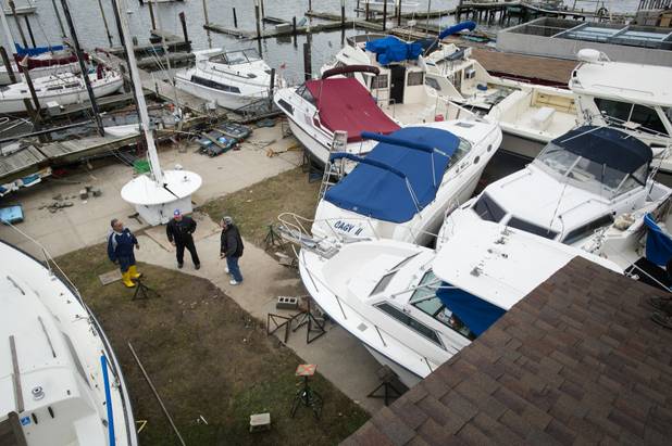 Members of the Varuna boat club stand near a pile of boats washed ashore, Wednesday, Oct. 31, 2012, in the Brooklyn borough of New York. Sandy, the storm that made landfall Monday, caused multiple fatalities, halted mass transit and cut power to more than 6 million homes and businesses. (AP Photo/ John Minchillo)