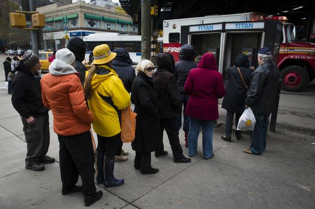 People wait to use a pay phone on Bright Beach Avenue, Wednesday, Oct. 31, 2012, in the Brooklyn borough of New York. People in the coastal corridor battered by superstorm Sandy took the first cautious steps Wednesday to reclaim routines upended by the disaster, even as rescuers combed neighborhoods strewn with debris and scarred by floods and fire. (AP Photo/ John Minchillo)