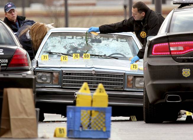 This Friday, Nov. 30, 2012, photo shows Ohio BCI agents and other law enforcement officials investigating a police shooting that killed two people in East Cleveland, Ohio. A chase that ended in 13 officers firing 137 rounds into a car, killing both people inside, began with a pop, perhaps a backfire from a car passing police headquarters or, as an officer suspected, a gunshot. 