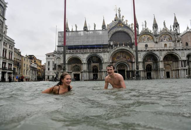 In this Nov. 11, 2012 file photo, a young man and a woman enjoy swimming in flooded St. Mark's Square in Venice, Italy. High tides flooded Venice, leading Venetians and tourists to don high boots and use wooden walkways to cross St. Mark's Square and other areas under water. 