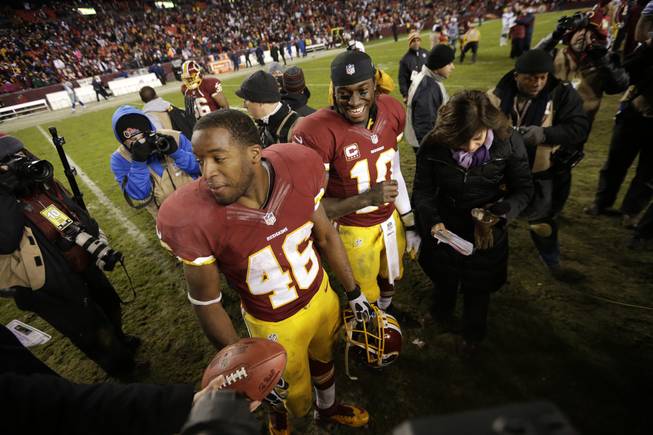 Washington Redskins quarterback Robert Griffin III,center, and teammate Alfred Morris wait to be interviewed after an NFL football game against the Dallas Cowboys on Sunday, Dec. 30, 2012, in Landover, Md. The Redskins won 28-18 to win the NFC East.