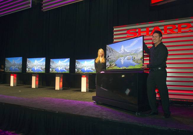 Models stand by a ICC Purios Ultra HD television at a Sharp press conference during the 2013 International CES in the Mandalay Bay Convention Center Monday, January 7, 2013. In the background are new Aquos 8-Series televisions and a 90-inch LED Smart 3D TV (far left). Sharp introduced new television technology and devices made with IGZO technology (Indium gallium zinc oxide) which promises ultra-high screen resolution with very low power usage.