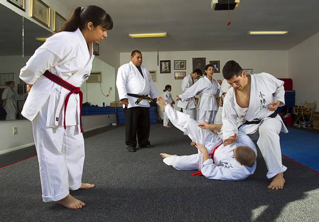 Student Abril Becerra, 14, looks on as Shorin-ryu karate instructor Andy Dowdell, a fifth degree black belt, demonstrates a take-down technique on student Mikel Hansen, 17, during a class at his home Sunday, Jan. 27, 2013. S