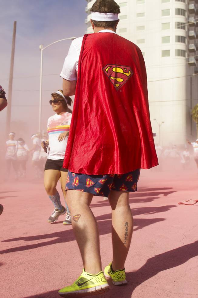 A participant wearing a superman cape and shorts with a superman tattoo on his left calf waits after passing the pink stage of the 5K Color Run, Saturday, Feb. 16, 2013. 