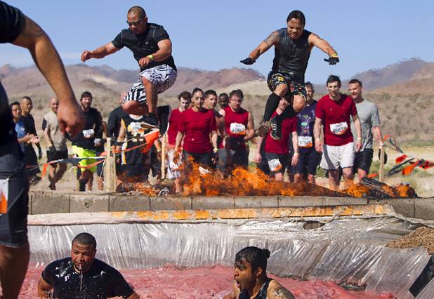 Competitors leap over fire into a water pit during the Tough Mudder in Beatty, Nev. Sunday, April 14, 2013. Tough Mudder events are hardcore 10-12 mile obstacle courses designed to test all-around strength, stamina, mental grit, and camaraderie.