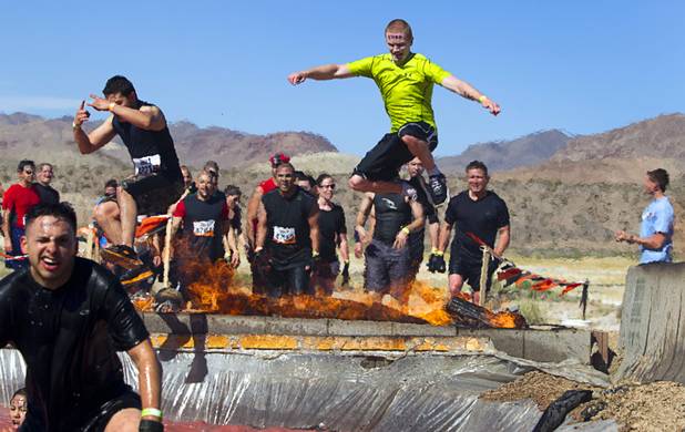 Competitors leap over fire into a water pit during the Tough Mudder in Beatty, Nev. Sunday, April 14, 2013. Tough Mudder events are hardcore 10-12 mile obstacle courses designed to test all-around strength, stamina, mental grit, and camaraderie.