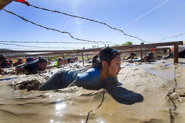 A woman crawls through the mud under barbed wire during the Tough Mudder in Beatty, Sunday, April 14, 2013. Tough Mudder events are hardcore 10-12 mile obstacle courses designed to test all-around strength, stamina, mental grit, and camaraderie.