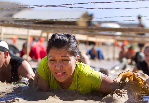 A woman crawls through the mud under barbed wire during the Tough Mudder in Beatty, Nev. Sunday, April 14, 2013. Tough Mudder events are hardcore 10-12 mile obstacle courses designed to test all-around strength, stamina, mental grit, and camaraderie.
