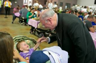 Bishop Joseph Pepe holds the hand of 11-month-old Mackyah during the Feast of Hope at the St. Vincent Lied Dining Facility at Catholic Charities of Southern Nevada, Thursday April 25, 2013.