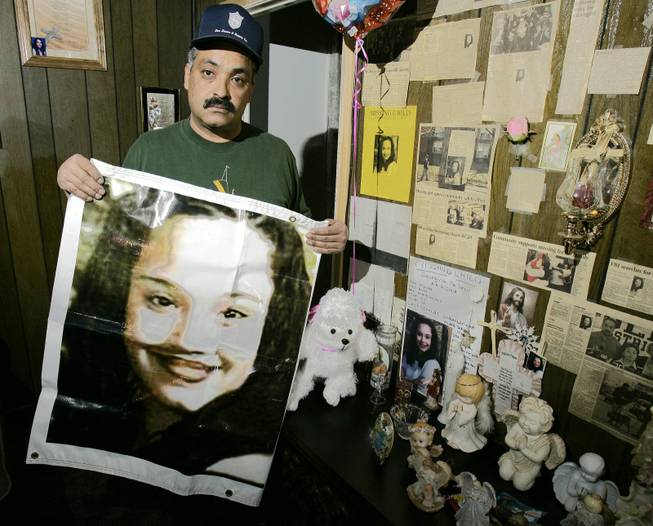 This March 3, 2004, file photo shows Felix DeJesus, holding a banner showing his daughter's photograph, standing by a memorial in his living room in Cleveland. 