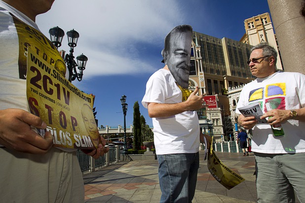 Justin McAffee, center, wears a Carlos Slim mask as he talks with tourist Tom Camasta of Chicago about Slim, a Mexican businessman listed as the second richest man in the world by Bloomberg's Billionaire Index, in front of the Venetian Wednesday, May 22, 2013. Two Countries One Voice accuses Slim's telecommunication companies of engaging in predatory and monopolistic practices. The protest coincides with CTIA, a wireless technology convention, being held at the Sands Expo Center.
