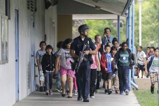 A Santa Monica police officer leads children on a field trip from Citizens of the World Charter School in Los Angeles out of Santa Monica College, where they had gone for a planetarium show, following a shooting in the area, in Santa Monica, Calif., Friday, June 7, 2013. 