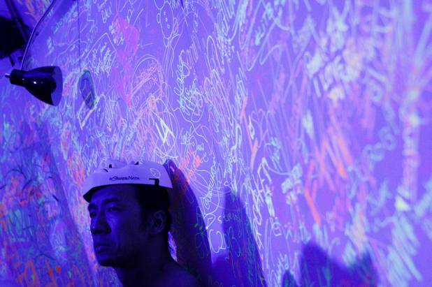 A festival goer watches on as visitors to the Sharpie Neon tent decorate their mask at the Electric Daisy Carnival Festival, EDC, at the Las Vegas Motor Speedway, Sunday morning, June 23, 2013.