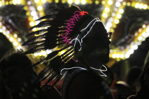 A festival goer wearing a lit up feather headdress waits in line for a carnival ride at the Electric Daisy Carnival Festival, EDC, at the Las Vegas Motor Speedway, Sunday morning, June 23, 2013.