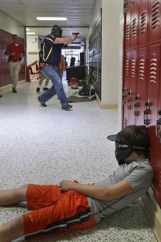In this photo taken July 11, 2013, a Clarksville schools faculty member, wearing a protective mask, rear center, carries a practice handgun toward a classroom in the city's high school in Clarksville, Ark., as students portray victims in a mock school shooting scenario. Twenty Clarksville School District staff members are training to be armed security guards on campus.