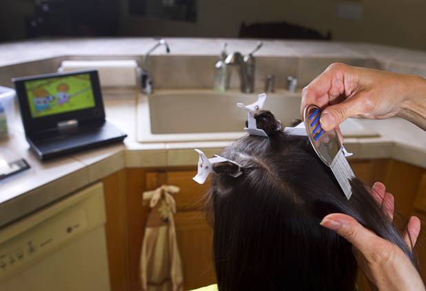 Michelle Lohrli, co-owner of Lice Happens, a mobile lice-removal service, demonstrates her technique on her daughter at her home Sunday, July 28, 2013. Having a portable DVD player keeps the child occupied while removing nits. The business is part of a national franchise system.