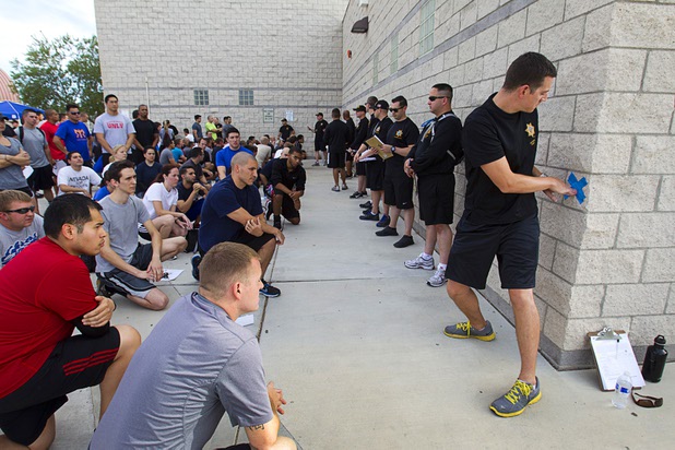 Metro Corrections Officer Jon Clark, right, demonstrates the proper technique for the "bend, twist and touch" drill during physical fitness testing for Metro Police recruit candidates at Cimarron-Memorial High School Thursday, Aug. 1, 2013