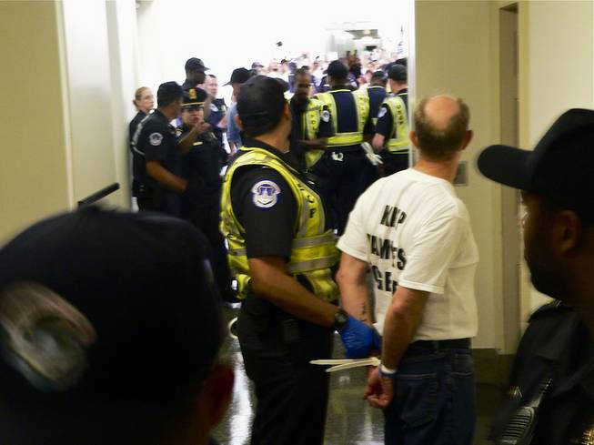 Bob Fulkerson, handcuffed, of PLAN, who was the first activist arrested Thursday, looks down a hallway of the Longworth House Office Building in Washington, D.C., to where Capitol Police are arresting other activists participating in a sit-in outside House Speaker John Boehner's district office Thursday, July 31, 2013.