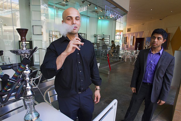 Tariq Ibraham, owner of Evapor8, a hookah lounge and vapor boutique, blows water vapor from an e-cigarette after a ribbon-cutting ceremony at Neonopolis in downtown Las Vegas Thursday, Aug. 8, 2013. Store manager Ahmed Tebha looks on at right.