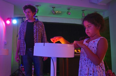 Artist David Sanchez Burr, left, watches as Katelyn Lopez, 8, of Long Beach, operates a control panel at the P3 Gallery in the Cosmopolitan Sunday, Aug. 25, 2013. The buttons on the panel create musical notes and vibrations that shake artwork that is placed on New Citadel platforms.