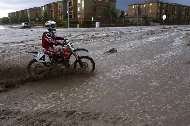A man rides a motocross motorcycle through storm runoff on Grand Teton Drive near Grand Canyon Drive Sunday, Aug. 25, 2013.