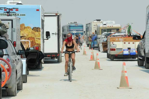 In this Aug. 26, 2013 photo, a woman rides her bike between cars waiting to enter Burning Man in Gerlach, Nev. According to The Reno Gazette-Journal, an estimated 68,000 people are anticipated to attend the event. 
