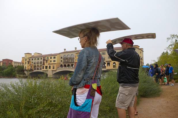 Spectators use signs as rain shelters during the start of the Ironman 70.3 World Championship at Las Las Vegas in Henderson Sunday, Sept. 8, 2013. More than 1,800 athletes from around the U.S. and 53 countries qualified for the event.