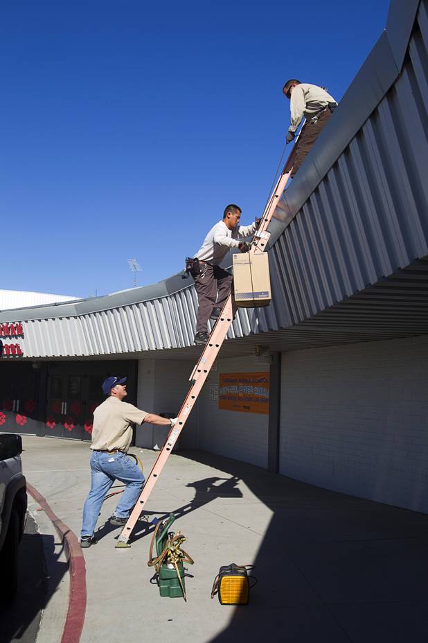 Stephen Molina, assists Tadone Phengrasamee as they take a new compressor to the roof of Cashman Middle School Tuesday, Sept. 17, 2013. Zone supervisor Gregg Peterson is at left. As the effects of the recession continue to affect school operations and deferred maintenance costs continue to rise, the CCSD is finding it difficult to maintain school facilities.